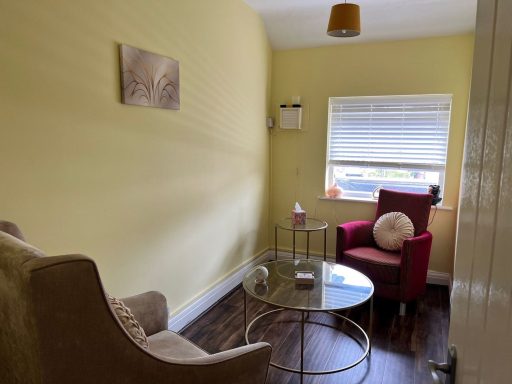 A small room with a yellow wall, a red armchair, a glass table, and an inviting atmosphere.